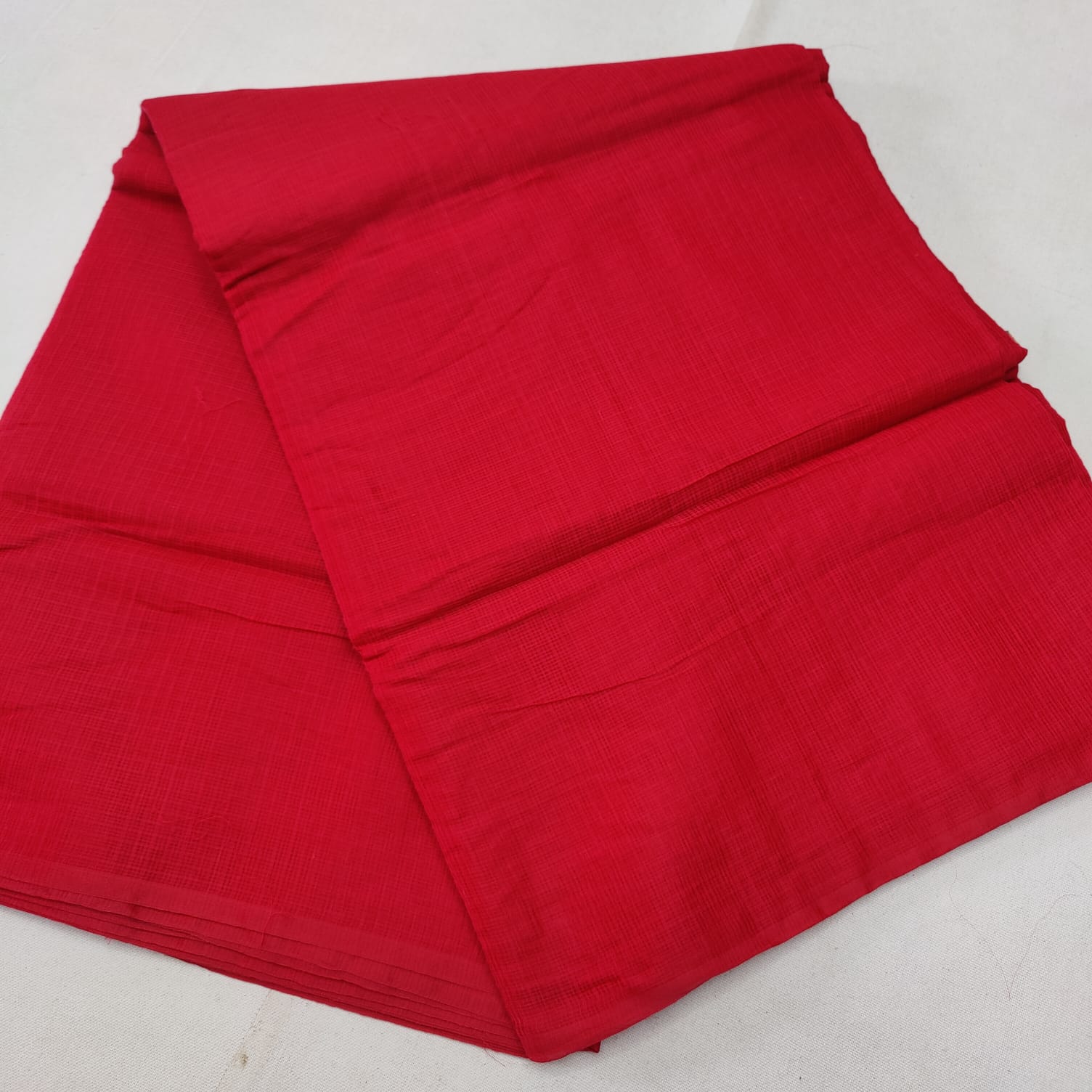 A folded red Kota cotton plain saree with a solid pattern, displayed on a white background.