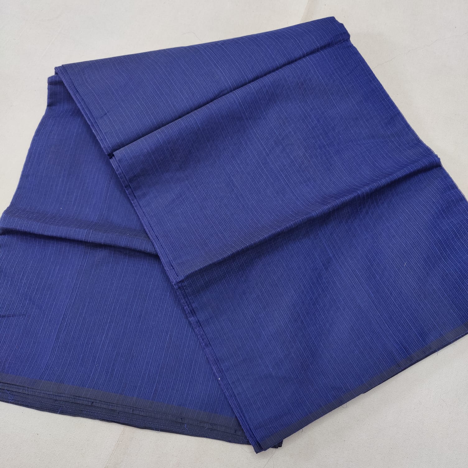 A folded blue Kota cotton plain saree with a solid pattern, displayed on a white background.