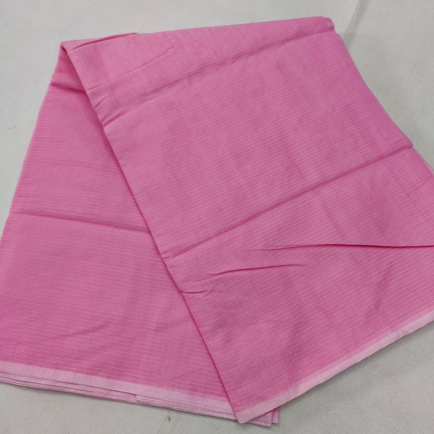 A folded pink Kota cotton plain saree with a solid pattern, displayed on a white background.