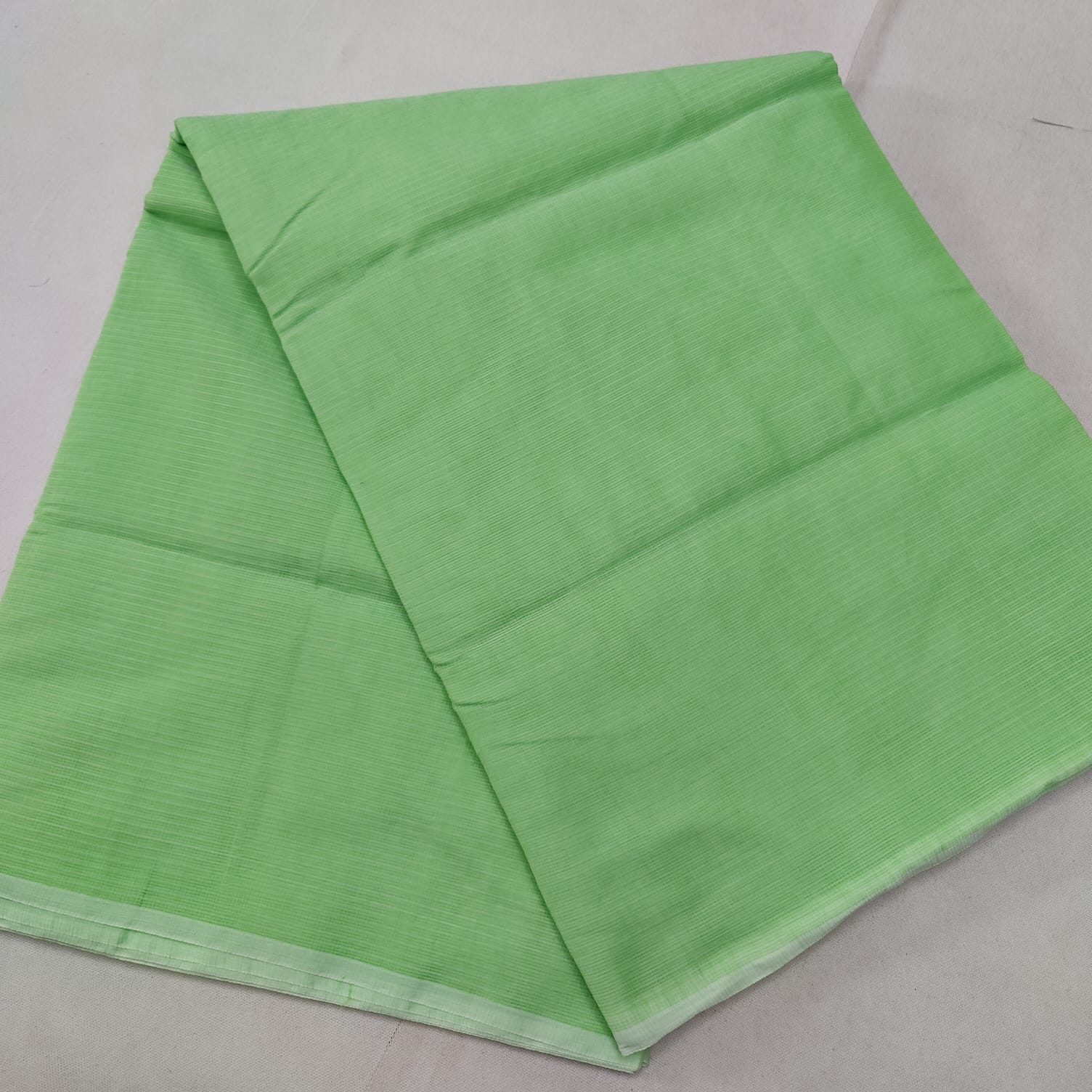 A folded Green Kota cotton plain saree with a solid pattern, displayed on a white background.