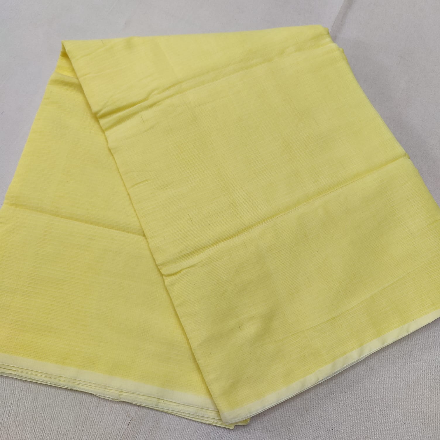 A folded Yellow Kota cotton plain saree with a solid pattern, displayed on a white background.