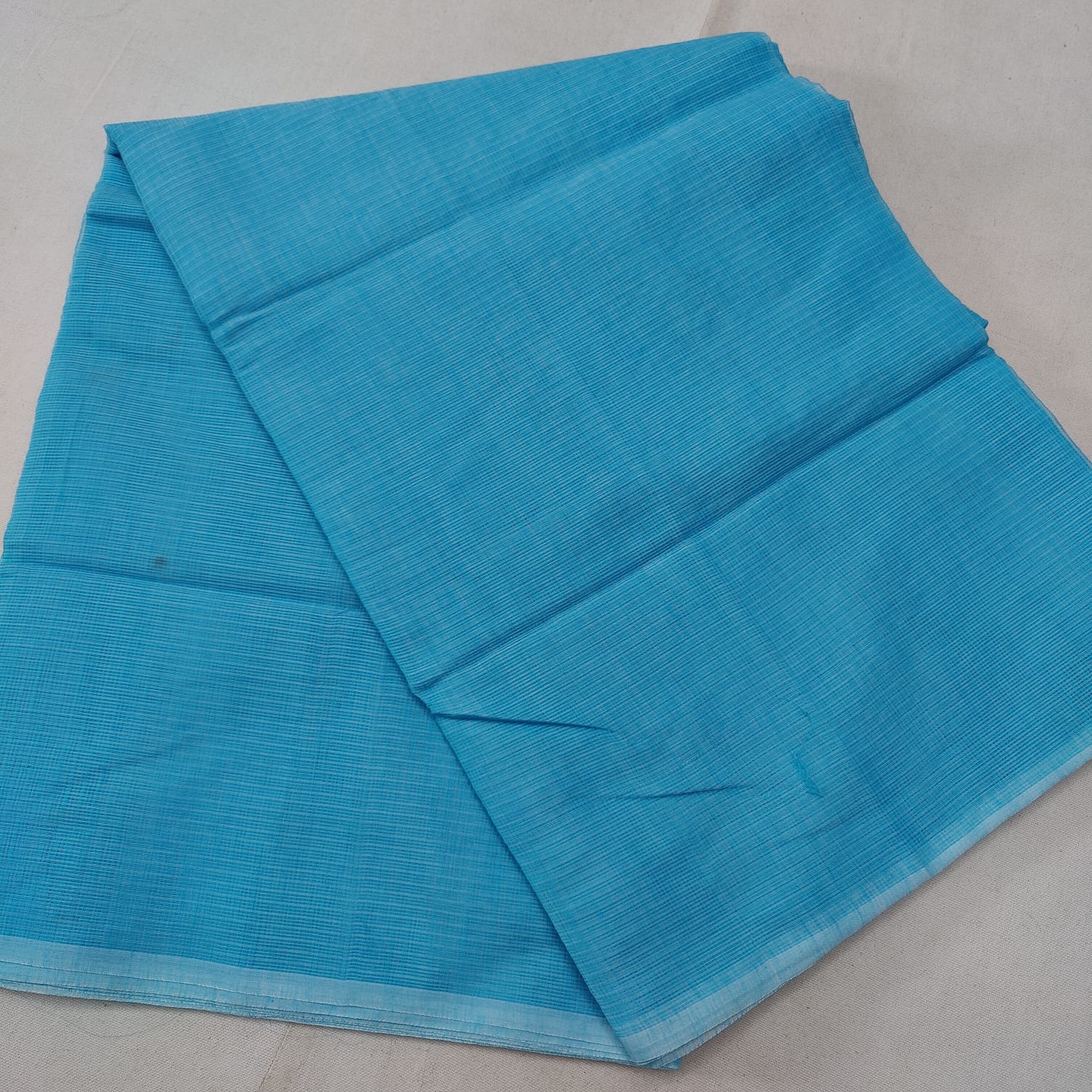 A folded blue Kota cotton plain saree with a solid pattern, displayed on a white background.