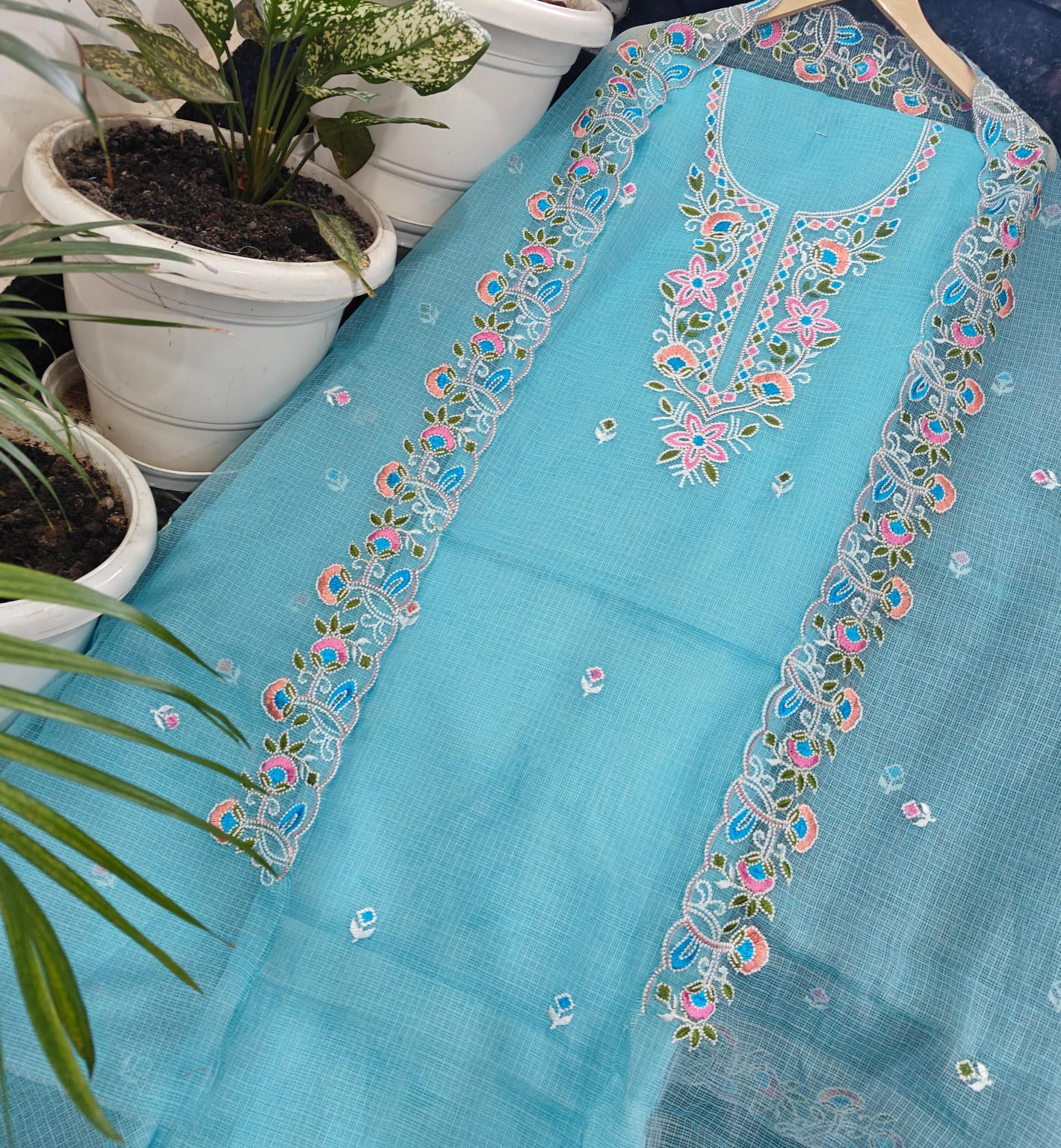 Kota Doria fabric with floral embroidery on a surface with potted plants in the background