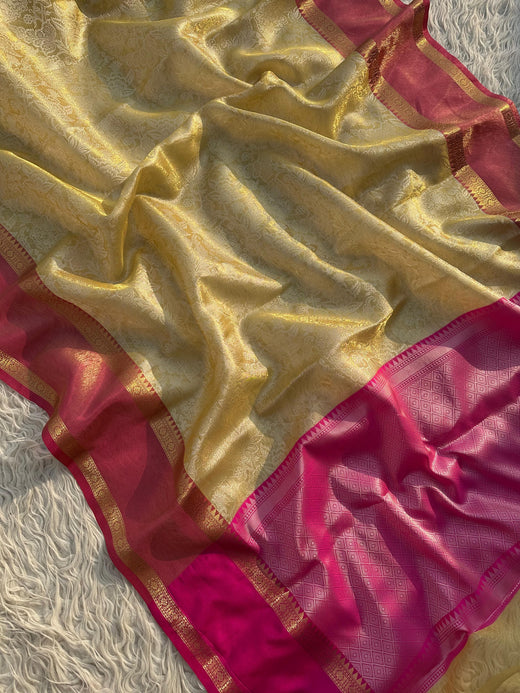 A Banarasi tissue silk saree in golden color with a pink border, displayed on a white background.
